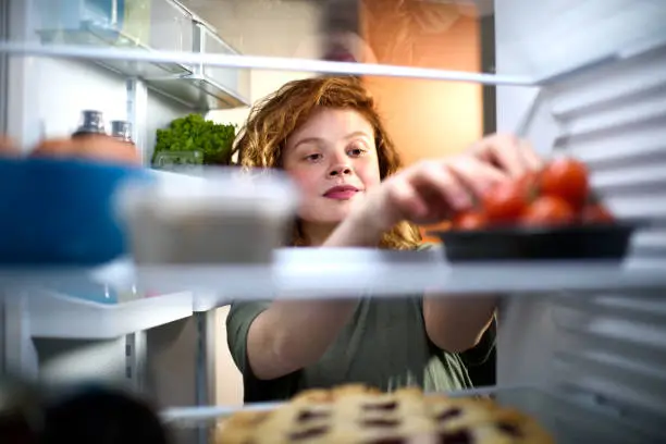 Woman looking inside the refrigerator and picking up cherry tomatoes.