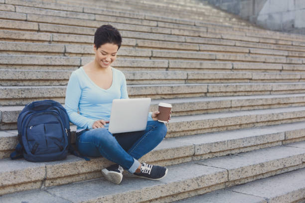 istock Young smiling female freelancer working on a laptop and drinking coffee outside 939117190