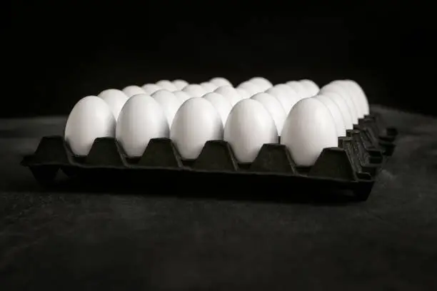 Photo of white eggs in a black carton tray