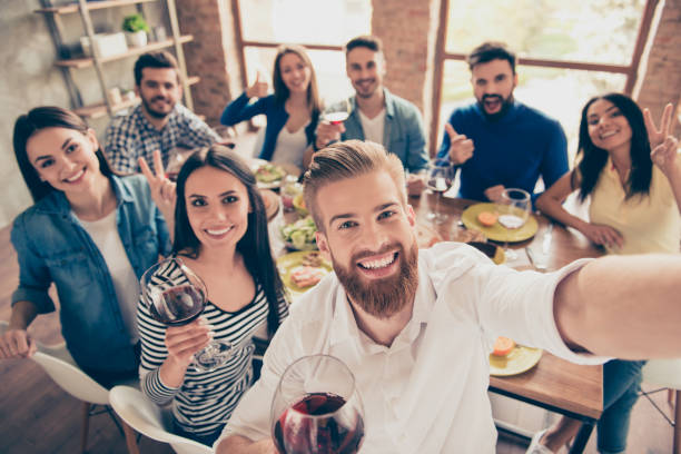 grupo multiétnico. bonitão barbudo está fazendo selfie com seus amigos na festa na câmera do seu telefone. todos estão sorrindo e e desfrutando de sua companhia, se divertindo - foodie - fotografias e filmes do acervo