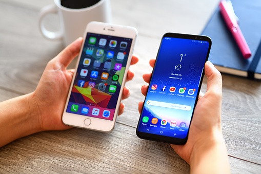 İstanbul, Turkey - March 7, 2018: Hand holding two smart phones on a wooden desk. The smart phones are an Samsung Galaxy S9 plus and iPhone 6 Plus.  Samsung Galaxy is a touchscreen smart phone produced by Samsung Electronics. Apple iPhone 6 plus is a touchscreen smart phone produced by Apple Inc.