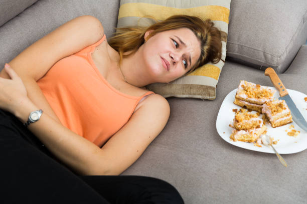 mujer es comer en exceso y sienta infeliz - comer demasiado fotografías e imágenes de stock