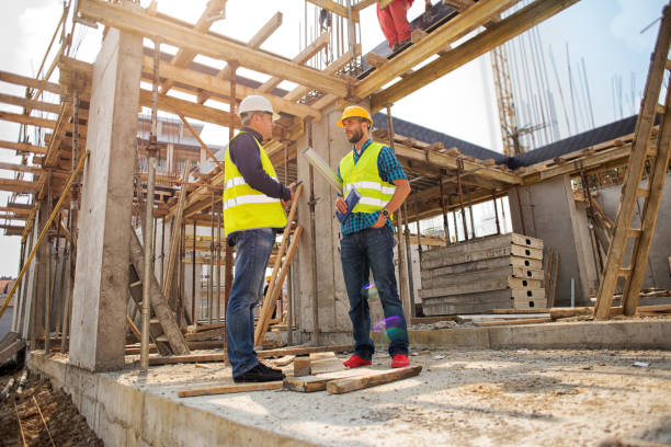 istock Man in hardhat and green jacket posing on building site 939155130
