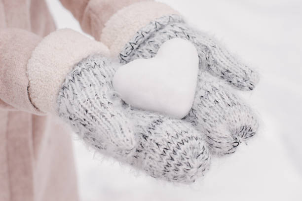 mãos em novelos de lã, segurando uma bola de neve em forma de coração. clima de inverno. símbolo de amor - glove winter wool touching - fotografias e filmes do acervo