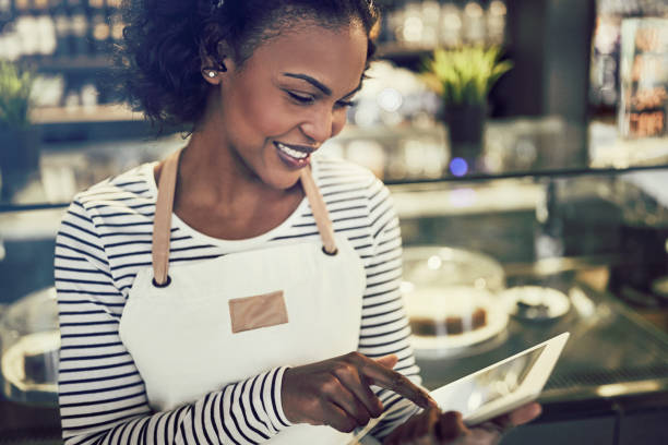 istock Smiling African entrepreneur using a tablet in her trendy cafe 939160050