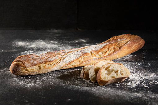 complete bread on black background with flour and three slices