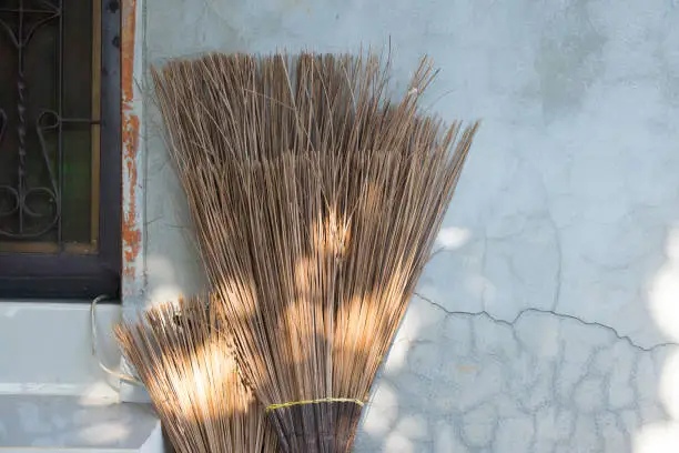Old styled broom made of coconut leaf and dry leaf on old wall