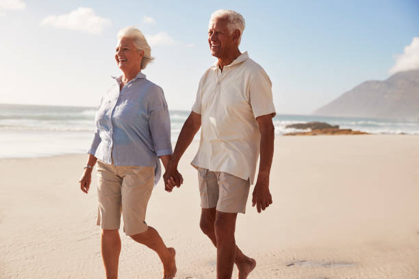 istock Senior Retired Couple Walking Along Beach Hand In Hand Together 939174146