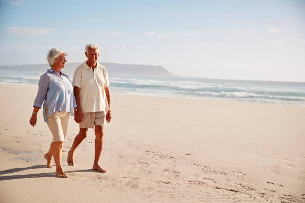 istock Senior Retired Couple Walking Along Beach Hand In Hand Together 939174154