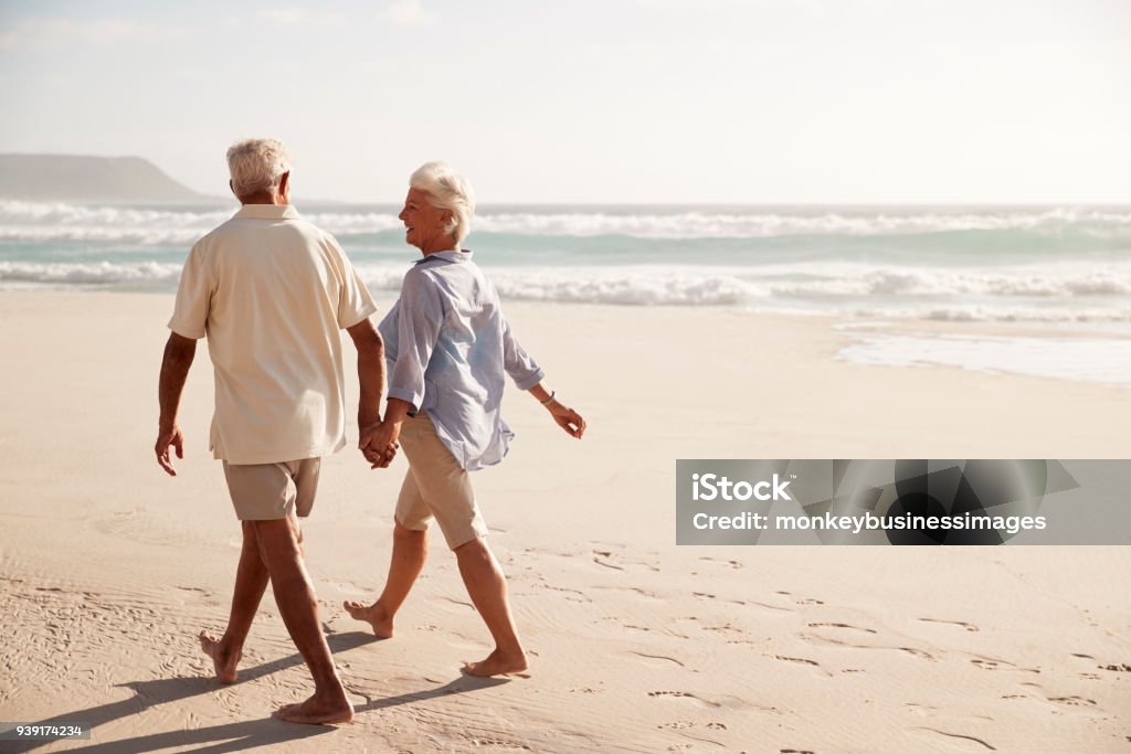 ビーチを手をつないで歩く老夫婦の後姿 - 浜辺のロイヤリティフリーストックフォト