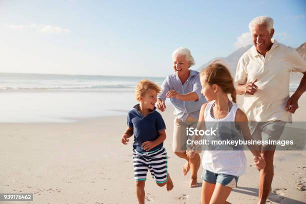 Nonni Che Corrono Lungo La Spiaggia Con I Nipoti Durante Le Vacanze Estive - Fotografie stock e altre immagini di Nonni