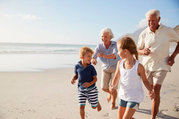 grandparents running along beach with grandchildren on summer vacation - neto imagens e fotografias de stock