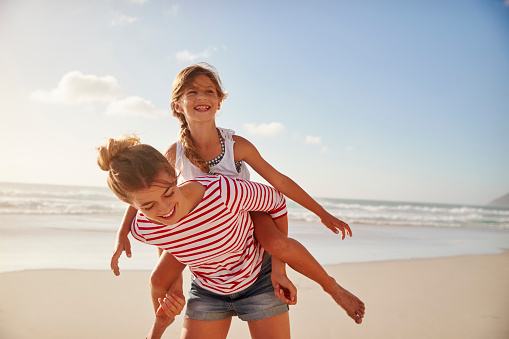 Mother Carrying Daughter On Shoulders On Beach Vacation