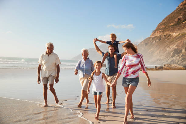 wielopokoleniowa rodzina na wakacjach spacerując razem wzdłuż plaży - multi family zdjęcia i obrazy z banku zdjęć