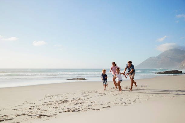 genitori che corrono lungo la spiaggia con i bambini durante le vacanze estive - family beach cheerful happiness foto e immagini stock