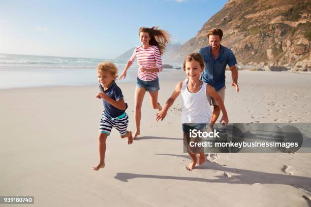 Parents Running Along Beach With Children On Summer Vacation Stock Photo - Download Image Now