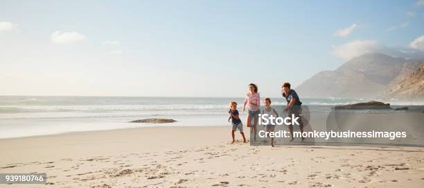 Genitori Che Corrono Lungo La Spiaggia Con I Bambini Durante Le Vacanze Estive - Fotografie stock e altre immagini di Famiglia