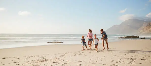 Photo of Parents Running Along Beach With Children On Summer Vacation