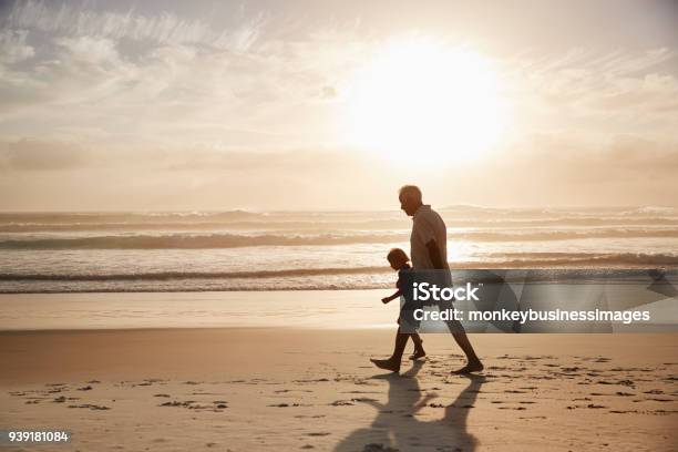 Silhouette Of Grandfather Walking Along Beach With Grandson Stock Photo - Download Image Now