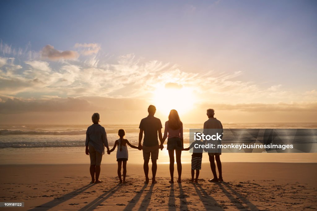 Rear View Of Multi Generation Family Silhouetted On Beach Family Stock Photo