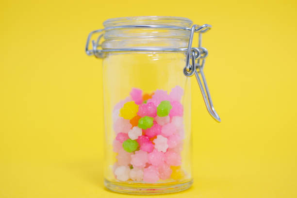 Colorful star shaped Japanese sugar candies, usually called konpeito in Japan, in a glass storage jar against yellow back ground.