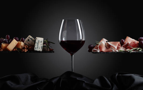 Glass of red wine with various cheeses , fruits and prosciutto .