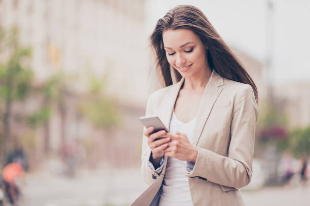 istock Young student is browsing on her pda while having a spring walk in the town outside, in a formal outfit, smiling, going to meet friend, wind plays with her hair 939197288