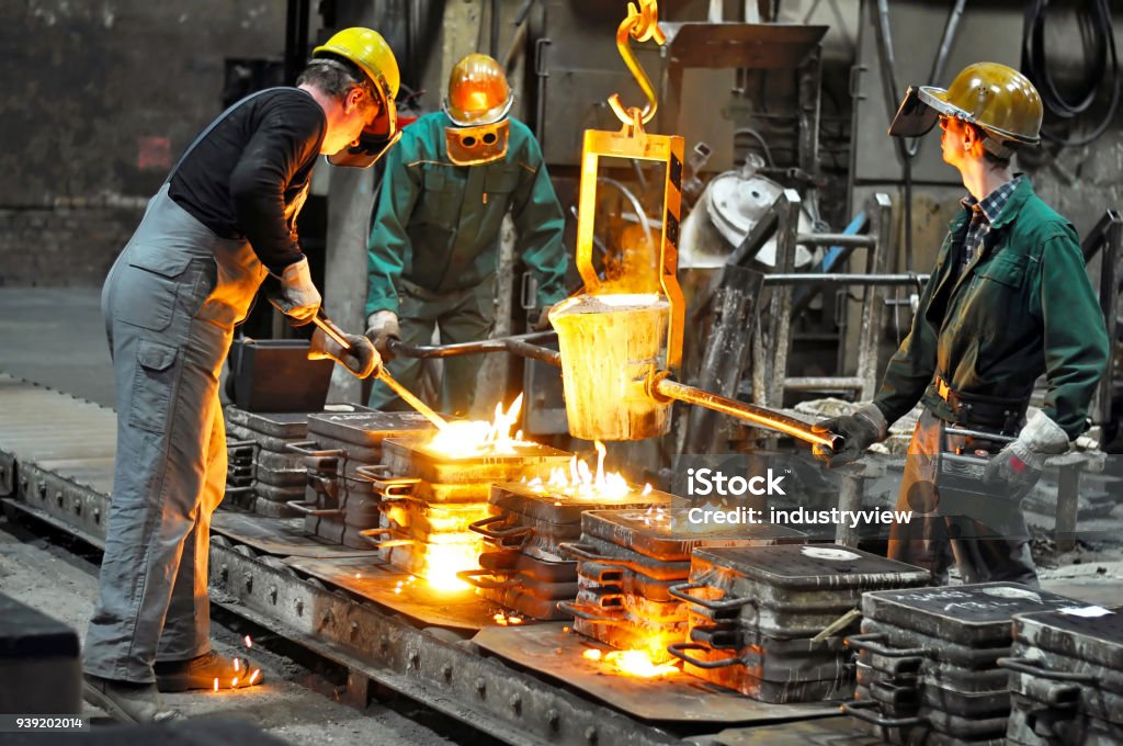 Group of workers in a foundry at the melting furnace - production of steel castings in an industrial company Industry Stock Photo