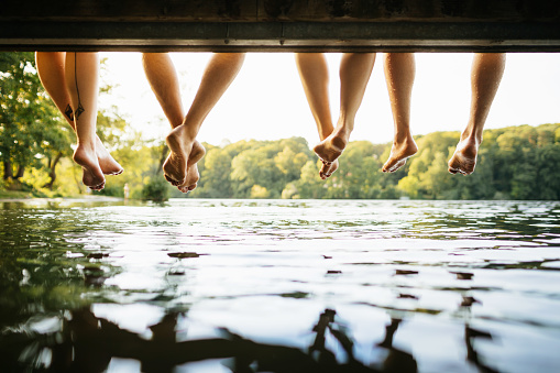 A group of friend’s dangling their legs together over the water at a lake.