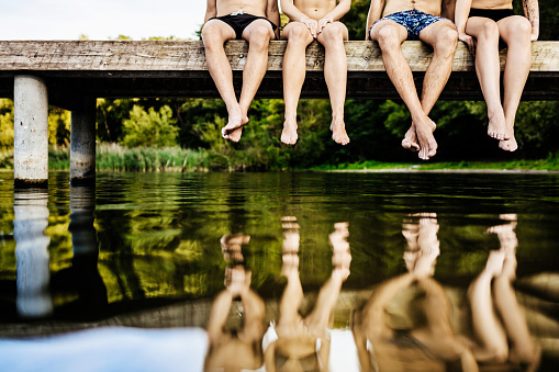 A group of friend’s dangling their legs together over the water at a lake.