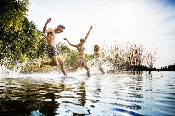 amigos chapoteando en agua en el lago juntos - jumping women running vitality fotografías e imágenes de stock
