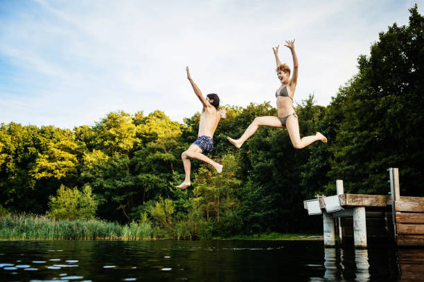 coppia che salta giù dal molo insieme in un lago - women action jumping running foto e immagini stock