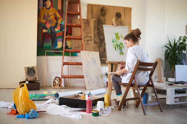 istock Artistic girl sitting in studio and paint on easel. 939217888