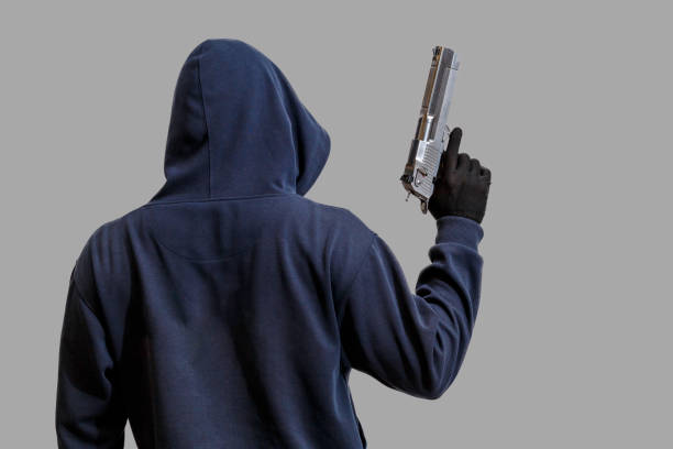 hombre encapuchado con un arma en la mano aislada sobre fondo gris - handgun gun blue black fotografías e imágenes de stock