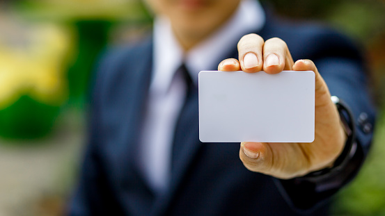 Young businessman hand holding blank white credit card mock up front side view, Empty plastic bank-card design mock up, white business name card mock up, money and finances concept