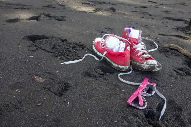 Sandy red shoes and girls sunglasses on Waipio Valley black sand beach, Hawaii big island.
