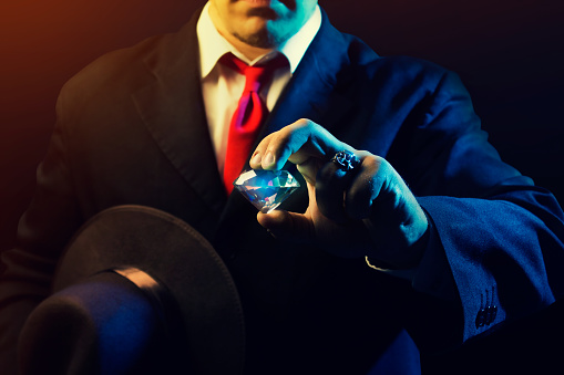 Mafia man holding hat & diamond on black background.