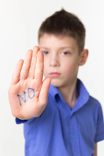 Teen little boy making stop sign with word no on open palm. Stop, reject, protest, object concept. Selective focus on open palm. Negative emotions concepts