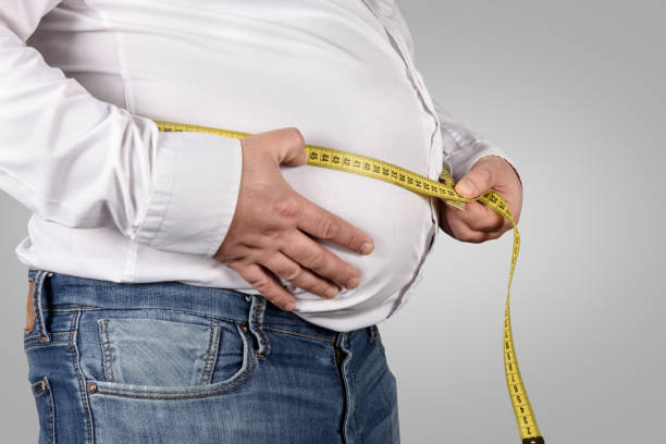 overweight man measuring his belly with tape measure - overweight men people abdomen imagens e fotografias de stock