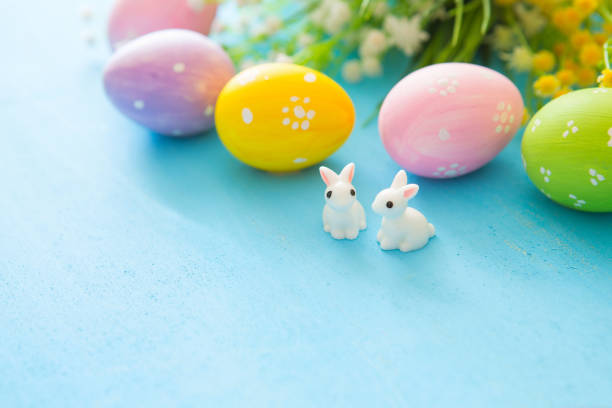 istock Beautiful Easter eggs with rabbits toy and flowers on blue wooden background, closeup. Easter holiday concept 939290864