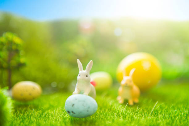 istock Happy Easter concept. Easter rabbits toy on spring green grass. Fairy tale sunset on the plastic green field with plastic grass, mushrooms and trees. Fake grass. Macro 939291590