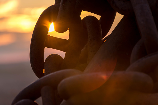 Sunset glowing through a link of an anchor chain of a boat