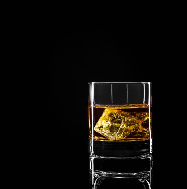 Whiskey glass with golden alcohol and ice cube on black background