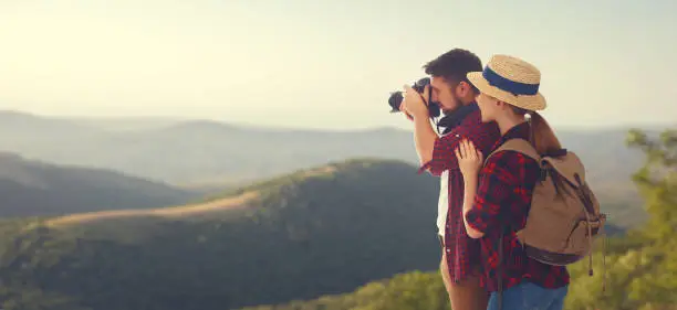 happy couple tourist with photo camera at top of mountain at sunset outdoors during a hike in summer