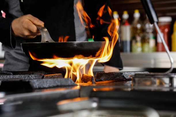 He Prepares Dish in a Pan with Open Flames