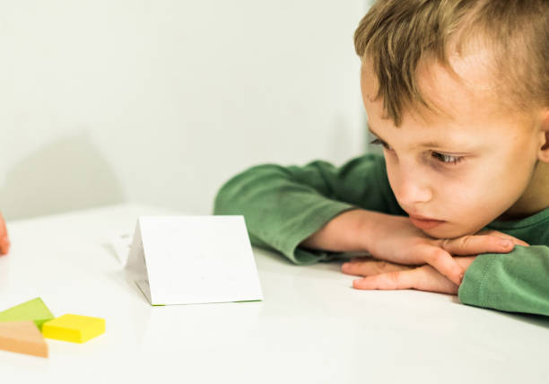 istock Cute boy with head on hands sitting at the table and thinking how to solve this puzzle 939316774