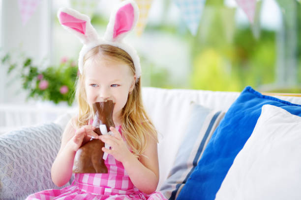 istock Cute little girl wearing bunny ears eating chocolate Easter rabbit 939325910