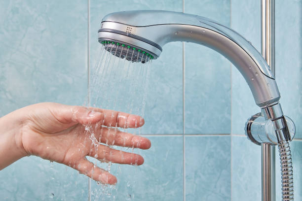 istock Hand under stream of water from shower head checks temperature. 939328562
