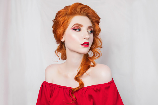 Beautiful red-haired girl in red dress posing on white background. Portrait of a woman with red hair