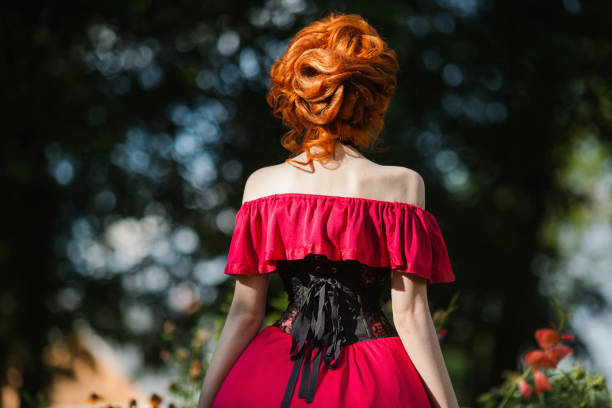 beautiful red-haired girl in a red dress and in black corset on a green background. a woman with red hair in a summer forest - espartilho imagens e fotografias de stock